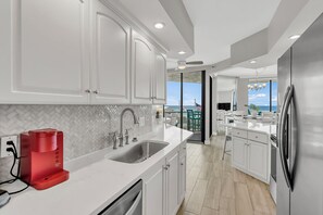 A modern kitchen with white cabinetry, a stainless steel refrigerator, and a view of the ocean through large windows. - 2 Free Beach SRVCS- 4 chairs/2 umbrellas! Free Beach Bonfires M/F nts (Miramar Beach)