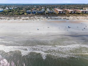 A beachfront hotel with multiple buildings, a sandy beach, and waves approaching the shore.