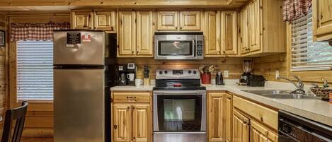 A wooden cabin kitchen with a refrigerator, microwave, stove, and sink.