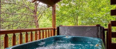 Een hottub op een houten terras, met uitzicht op weelderige groene begroeiing.