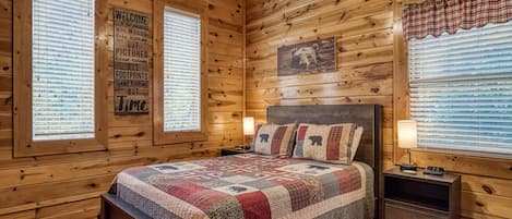 Un dormitorio rústico de cabaña de madera con una cama grande, dos mesitas de noche y un ventilador de techo.