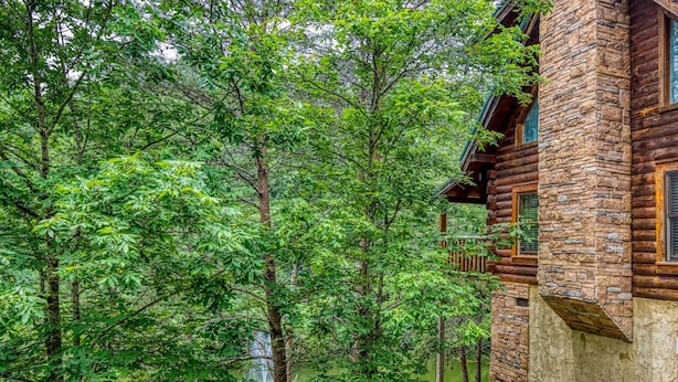 A log cabin with stone walls, surrounded by lush greenery and a pond. - ERN834 - LAKESIDE GETAWAY - GREAT LOCATION!  CLOSE TO ALL THE ACTION! (Pigeon Forge)