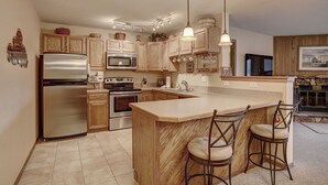 A kitchen with wooden cabinets, stainless steel appliances, a central island with bar stools, and pendant lighting. - Centrally Located/Walk to Lifts/Pool and Hot Tub Access/Private Patio (Keystone)