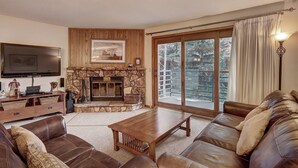 A living room with a stone fireplace, leather sofas, a flat-screen TV, and a large window with curtains. - Centrally Located/Walk to Lifts/Pool and Hot Tub Access/Private Patio (Keystone)