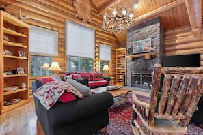 A log cabin interior with a fireplace, wooden shelves, a sofa, and a chandelier. - Abode on Obsidian, best value in Teton Village (Teton Village)