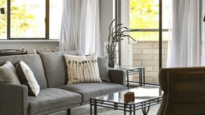 A modern living room with a gray sofa, a glass coffee table, and a view through large windows. - Beacon Hill View Condo (Victoria)