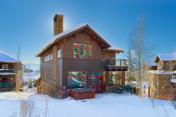Una cabaña de madera de dos pisos con ventanas grandes y un balcón, rodeada de nieve.
