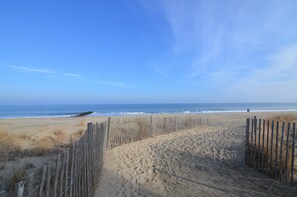 Une plage de sable bordée d’une clôture en bois, sous un ciel bleu et dégagé.