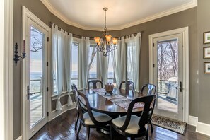 A dining room with a large table, chairs, a chandelier, and large windows with curtains. - View House  - Stunning Views of Mountains and Yadkin River, huge deck, wood burning fireplace (Boone)