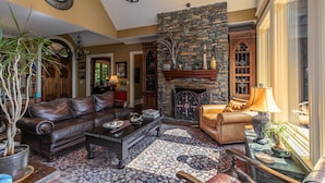 A cozy living room with a stone fireplace, leather sofas, and a large window. - View House  - Stunning Views of Mountains and Yadkin River, huge deck, wood burning fireplace (Boone)