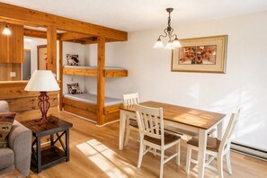 Une pièce chaleureuse avec un lit superposé, une table à manger en bois avec des chaises, une lampe et un tableau encadré au mur.