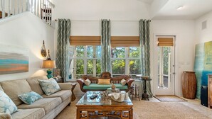 A cozy living room with a sofa, a coffee table, and a view of the outdoors through large windows.