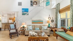A spacious living area with a high ceiling, a staircase, and a view of the kitchen.