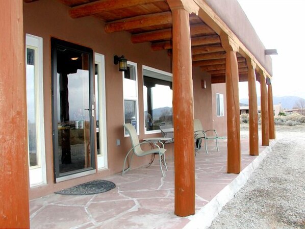 Un espacio exterior cubierto con suelo de piedra, pilares de madera y puertas de cristal que dan a un patio.
