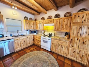 Een keuken met houten kastjes, een magnetron, fornuis en een klok aan de muur.