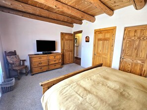Un dormitorio con una cama de madera, un televisor sobre un aparador de madera y puertas de madera.