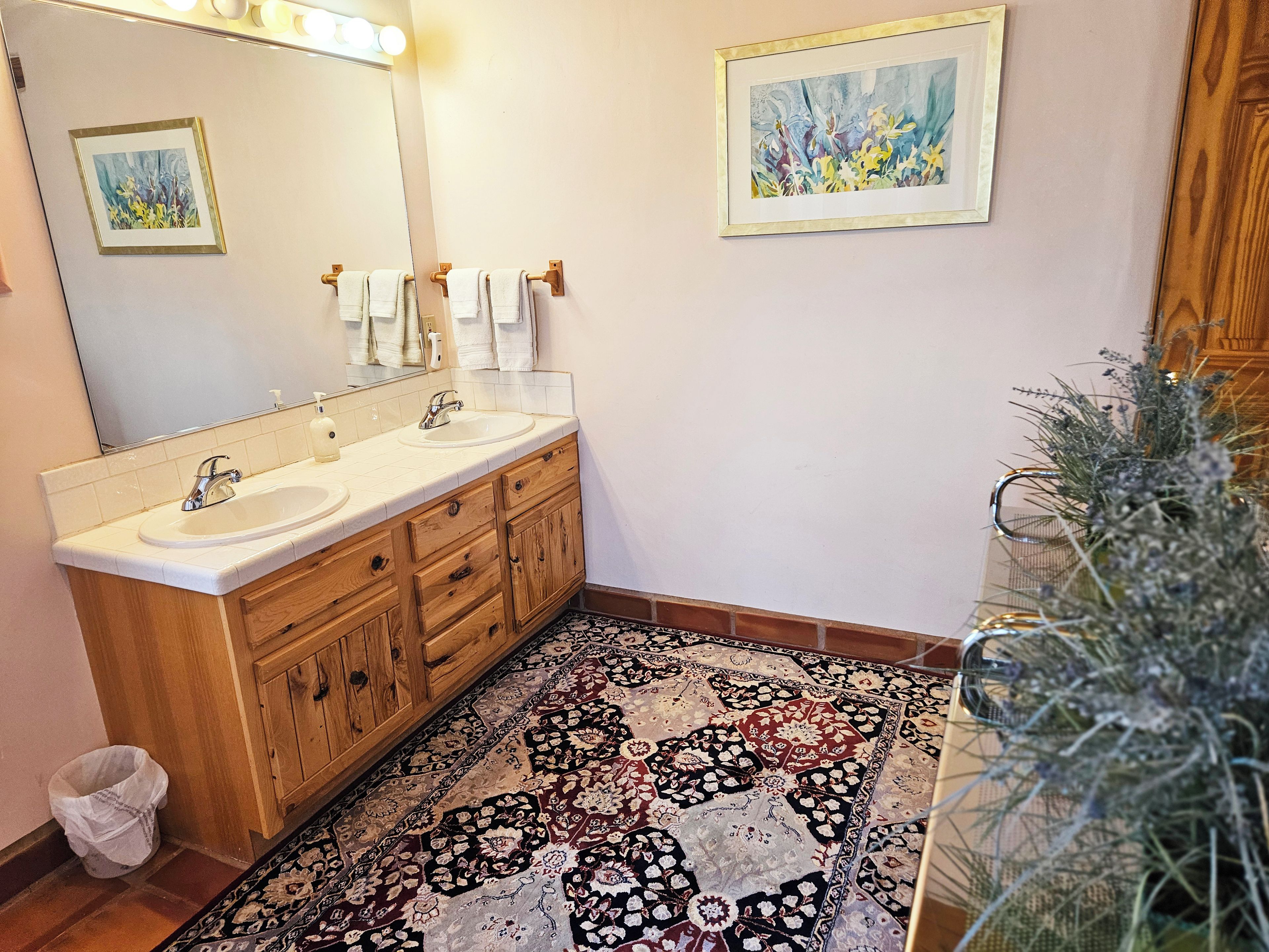 Une salle de bain avec deux lavabos, des meubles en bois, un grand miroir et un tapis à motifs.