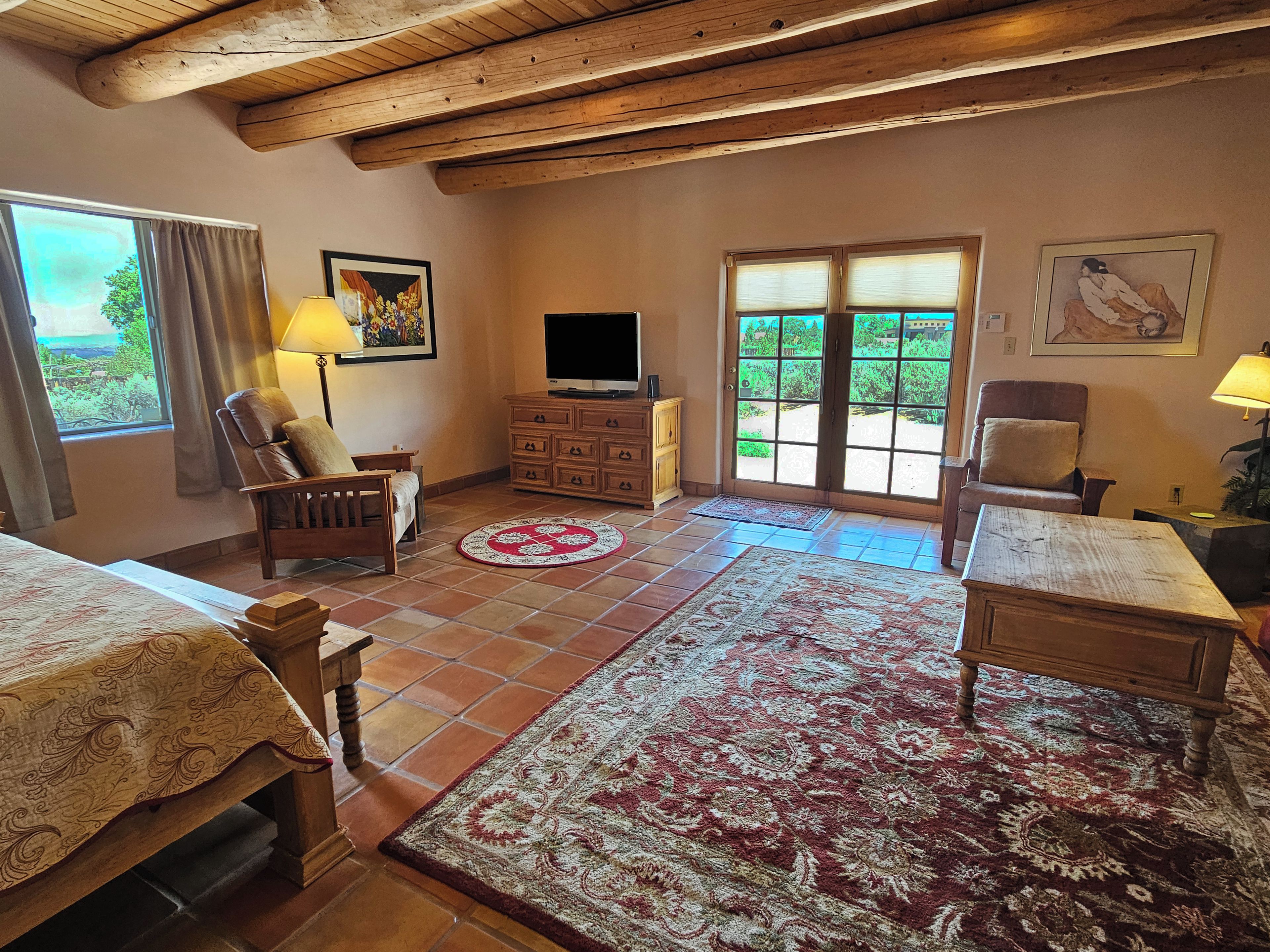 Una stanza con soffitto in legno, televisione, divano, una sedia e un tappeto decorato.