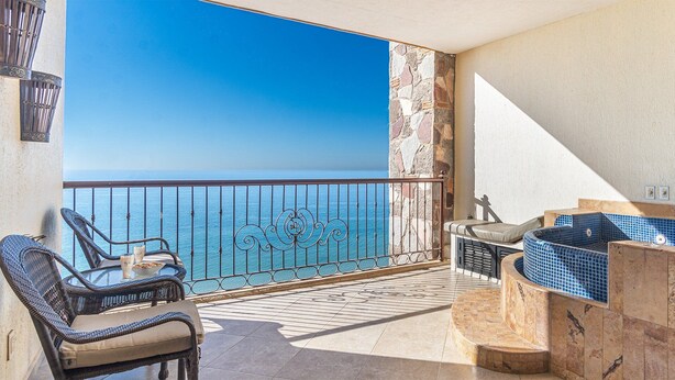 Un balcon agrémenté de meubles en osier, un mur en pierre et une vue sur la mer.