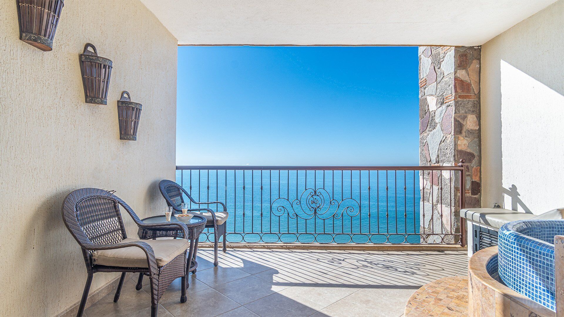 A balcony with wicker chairs, a small table, and a hot tub.
