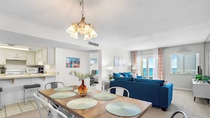 Eine moderne Küche mit weißen Schränken, einem Holztisch mit Platzdeckchen und einem blauen Sofa im Wohnbereich.