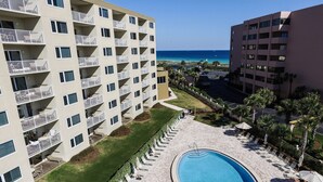 A pool area with lounge chairs and a swimming pool, surrounded by multi-story buildings with balconies. - The Islander 110 - Winter Months Available - Heated Pool (Destin)