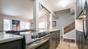 A modern kitchen with stainless steel appliances, a large island, and a view of the living area. - JHRL - Balsam Lodge A8 - Great Location in the Aspens (Wilson)