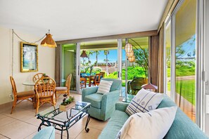 Ein modernes Wohnzimmer mit Glastür zum Balkon, ausgestattet mit einer Couch, Sesseln und einem Tisch.