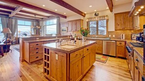 A spacious kitchen with wooden cabinets, a large island, and a view of the outdoors. - JHRL - Amazing 5-bedroom Granite Ridge Lodge #16, Hot Tub and Sweeping Views (Teton Village)