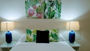 A hotel room with a bed, two nightstands, two lamps, and a tropical-themed wall art above the bed.