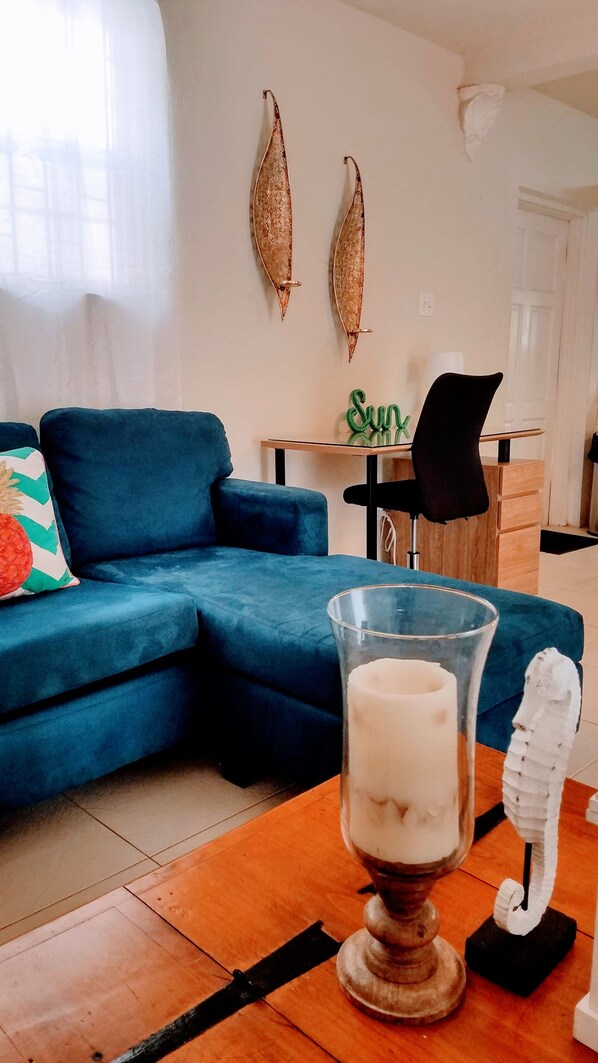 A living room with a blue sofa, a glass table with a white candle, and decorative items on the wall. - Mangoville Near Dover Beach (Oistins)