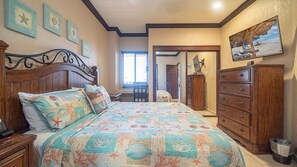 A bedroom with a large bed, wooden dresser, and a view of the beach through a window.