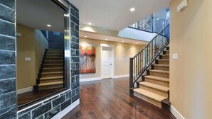A spacious hallway with a wooden staircase, a stone accent wall, and a painting on the wall. - Nature's Gate Executive Estate (Victoria)