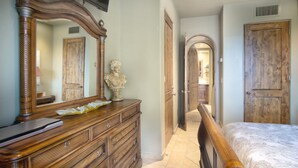 Un dormitorio con un aparador de madera, un espejo grande, una cama con cabecera de madera y una puerta que da a otra habitación.