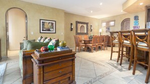 Amplia sala de estar con un sofá verde, mesa de centro de madera y una zona de comedor con sillas y mesa de madera.