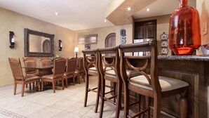 Un comedor con sillas de madera y una mesa de vidrio, un espejo grande y un jarrón decorativo.