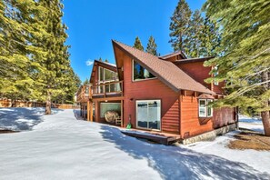 A two-story wooden cabin with a sloped roof, large windows, and a covered porch area.