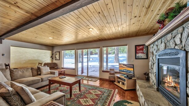Una sala de estar acogedora con chimenea de piedra, techo de madera, ventanas amplias y un espacio de descanso confortable.