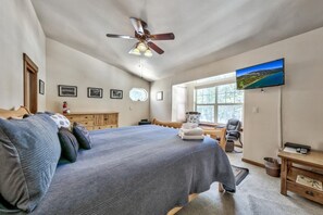 Ein Schlafzimmer mit einem Bett, einem Deckenventilator, einem Fernseher und einem Fenster.