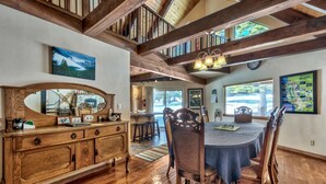 Comedor con mesa y sillas de madera, un espejo grande y vistas al exterior a través de amplias ventanas.