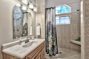A bathroom with a vanity, a shower, and a window with a view.