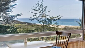 Een balkon met een houten tafel en stoel, met uitzicht op een strand en de oceaan.