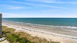 A beach with a row of umbrellas and a high-rise building in the background. - $150 activities - E-gift card when you book - Extra Deep Oceanfront Balcony | M1606 (Myrtle Beach)