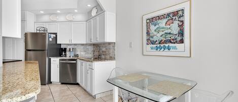 A modern kitchen with white cabinets, stainless steel appliances, and a glass dining table.