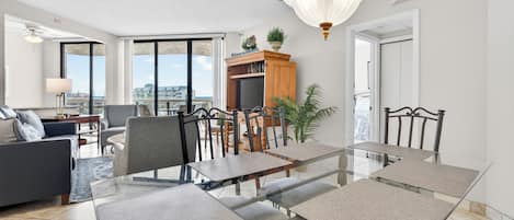 A modern living room with a glass dining table, comfortable seating, a bookshelf, and a view of the city.