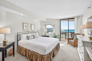Une chambre à coucher comprenant un lit, des tables de chevet, une commode, une chaise, une fenêtre avec vue et un balcon.