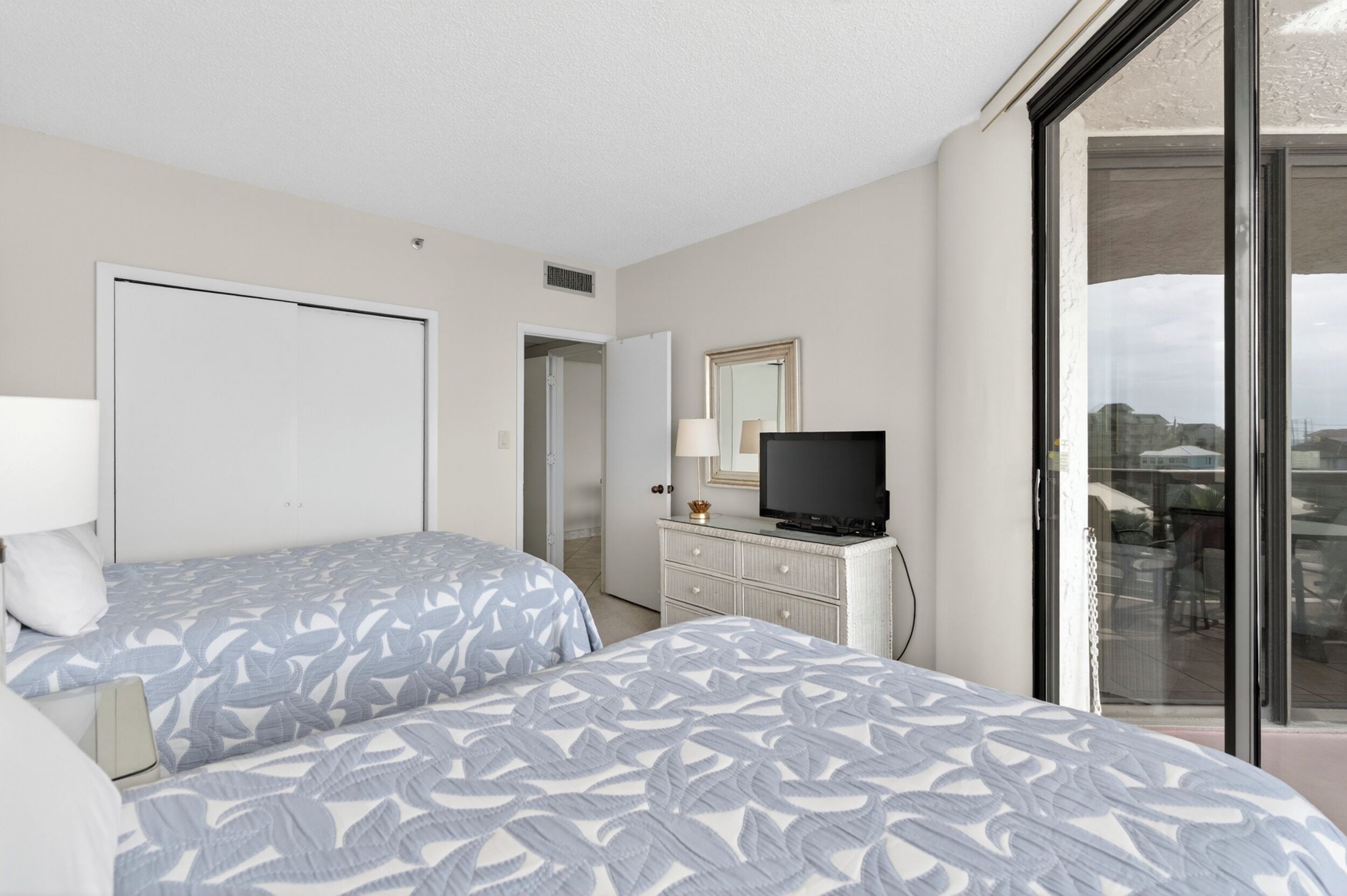 Een hotelkamer met twee bedden, een televisie, een dressoir en een schuifdeur naar een balkon.