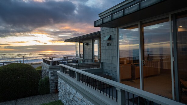 Un edificio moderno con balcón y vistas al océano, amplias ventanas de vidrio y fachada de piedra.