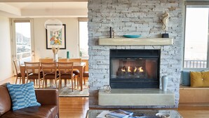 Una sala de estar con chimenea de piedra, un sofá de cuero marrón y una zona de comedor con sillas de madera.