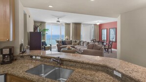 A modern kitchen with granite countertops, a double sink, and a dining area with a view of the ocean. - 0602 - Modern Gulf Front Oasis (Panama City Beach)